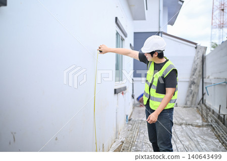 Asian Construction Inspector Measuring Wall with Tape Measure at Building Site Asian Construction Inspector Measuring Wall with Tape Measure at Building Site 140643499