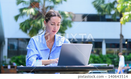 Woman working on laptop by pool in outdoor remote workspace setting Woman working on laptop by pool in outdoor remote workspace setting 140643514