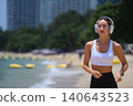 Active woman in white sports bra exercising and listening to music at the shore 140643523