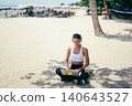 Side view of fit woman using laptop while sitting on the sand at a tropical beach 140643527