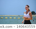 Fit woman running along beach wearing headphones, outdoor fitness and active lifestyle with ocean view 140643559