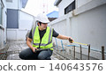 Construction Inspector Measuring Wall with Tape Measure and Tablet at Building Site 140643576