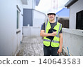 Young Asian Male Construction Inspector Smiling at Building Site Wearing Safety Vest and Hard Hat with Clipboard 140643583