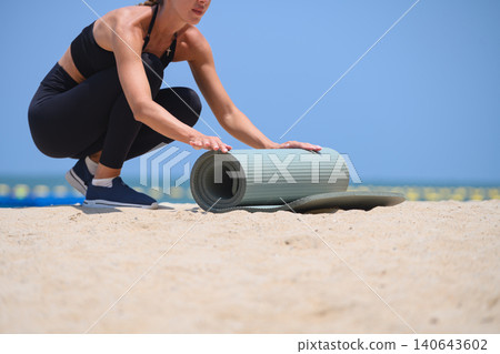 Closeup woman preparing yoga mat on sandy beach, outdoor workout and wellness lifestyle with calm ocean horizon Closeup woman preparing yoga mat on sandy beach, outdoor workout and wellness lifestyle with calm ocean horizon 140643602