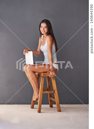 Laptop, portrait and smile of woman on chair in studio with gray wall background for social media. Computer, relax and underwear with happy young person sitting on stool for blogging or streaming Laptop, portrait and smile of woman on chair in studio with gray wall background for social media. Computer, relax and underwear with happy young person sitting on stool for blogging or streaming 140644390