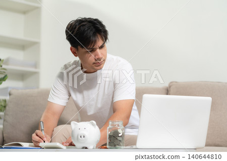 Serious young man sit at workplace desk use calculator calculates monthly expenses. Serious young man sit at workplace desk use calculator calculates monthly expenses. 140644810