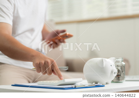 Concept with saving money, man working on desk in home using calculator and laptop to calculate budget. Concept with saving money, man working on desk in home using calculator and laptop to calculate budget. 140644822