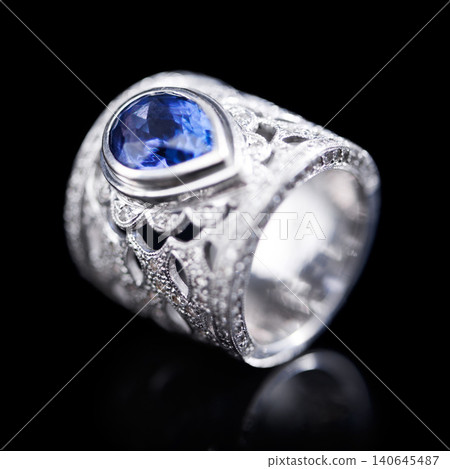Gemstone, silver and ring on a black background of luxury or expensive present for engagement or marriage in studio. Jewelry, diamonds and blue or sapphire rock in closeup, reflection and accessory Gemstone, silver and ring on a black background of luxury or expensive present for engagement or marriage in studio. Jewelry, diamonds and blue or sapphire rock in closeup, reflection and accessory 140645487