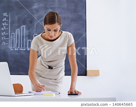Teacher, woman and writing for marking in classroom with ideas for planning, exam or review at desk. Person, computer and notes in book for feedback, results or test for education, learning or school 140645665