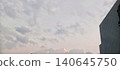 The afternoon sky is filled with thin gray and faded orange clouds. In the right corner is the side of a modern gray building with a checkered pattern. A calm atmosphere, soft light approaching evenin 140645750