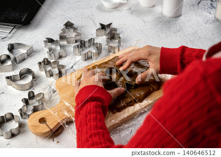 Person in a red sweater using a gingerbread man cookie cutter on spiced dough, preparing festive homemade Christmas treats Person in a red sweater using a gingerbread man cookie cutter on spiced dough, preparing festive homemade Christmas treats 140646512