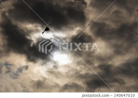 Helicopter silhouetted against dramatic stormy sky flying Helicopter silhouetted against dramatic stormy sky flying 140647010