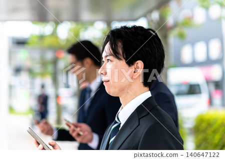 A man in a suit waiting for a bus at a bus stop. A man in a suit waiting for a bus at a bus stop. 140647122