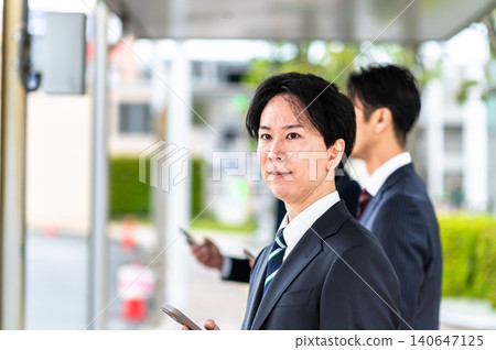 A man in a suit waiting for a bus at a bus stop. A man in a suit waiting for a bus at a bus stop. 140647125