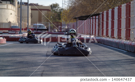 Thrilling go-kart race on vibrant track with helmets, red-white barriers, and scenic background. racing and adventure concepts. Thrilling go-kart race on vibrant track with helmets, red-white barriers, and scenic background. racing and adventure concepts. 140647437