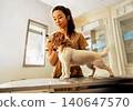 Trusted Pet Care Young Asian Female Vet in Tan Scrubs Gently Examines Small Jack Russell Terrier on Clinic Table from Low Angle 140647570