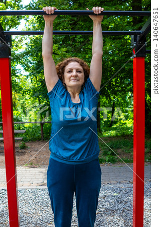 Mature woman doing pullup exercise on outdoor bar in park demonstrating fitness and strength Mature woman doing pullup exercise on outdoor bar in park demonstrating fitness and strength 140647651