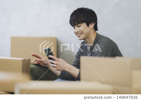 A young man holding a smartphone surrounded by cardboard boxes - Moving image 140647836