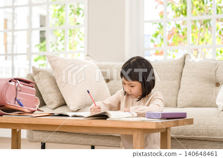 A young elementary school girl studying in her notebook in the living room. A young elementary school girl studying in her notebook in the living room. 140648461