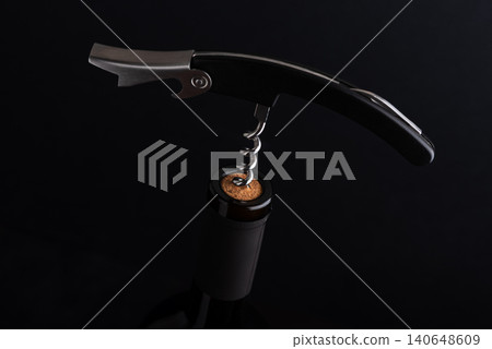 Corkscrew removing cork from a dark wine bottle 140648609