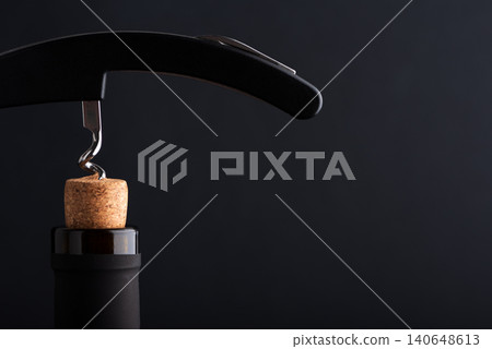 Corkscrew opening wine bottle with a cork on a dark background 140648613