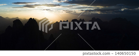 Panoramic view of the Dolomites at sunset with dramatic mountain silhouettes, golden light rays and storm clouds. Atmospheric alpine landscape captured from an aerial perspective. Panoramic view of the Dolomites at sunset with dramatic mountain silhouettes, golden light rays and storm clouds. Atmospheric alpine landscape captured from an aerial perspective. 140650150