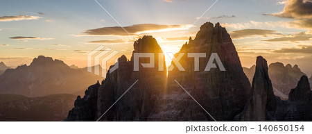 Spectacular sunset over Tre Cime di Lavaredo in the Italian Dolomites. Golden sunburst shines between iconic limestone peaks, creating a dramatic alpine mountain landscape. Spectacular sunset over Tre Cime di Lavaredo in the Italian Dolomites. Golden sunburst shines between iconic limestone peaks, creating a dramatic alpine mountain landscape. 140650154