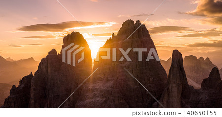 Spectacular sunset over Tre Cime di Lavaredo in the Italian Dolomites. Golden sunburst shines between iconic limestone peaks, creating a dramatic alpine mountain landscape. Spectacular sunset over Tre Cime di Lavaredo in the Italian Dolomites. Golden sunburst shines between iconic limestone peaks, creating a dramatic alpine mountain landscape. 140650155