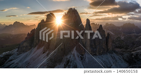 Spectacular sunset over Tre Cime di Lavaredo in the Italian Dolomites. Golden sunburst shines between iconic limestone peaks, creating a dramatic alpine mountain landscape. Spectacular sunset over Tre Cime di Lavaredo in the Italian Dolomites. Golden sunburst shines between iconic limestone peaks, creating a dramatic alpine mountain landscape. 140650158