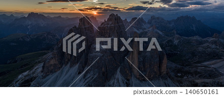 Spectacular sunset over Tre Cime di Lavaredo in the Italian Dolomites. Golden sunburst shines between iconic limestone peaks, creating a dramatic alpine mountain landscape. 140650161