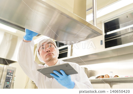A male staff member in a white coat conducts a hygiene check in the kitchen. 140650420