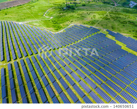 Hillside solar installations integrate seamlessly with lush fields. Aerial view showcasing renewable energy infrastructure harmoniously embedded in pastoral terrain 140650651