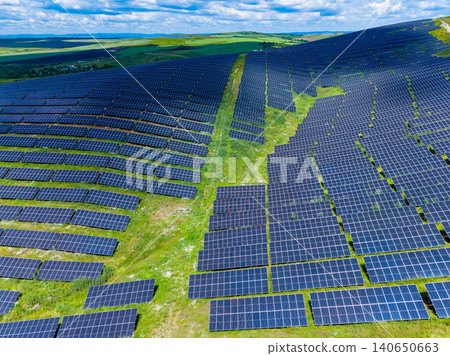 Photovoltaic installations stretching across undulating rural terrain under bright sky. Expansive renewable energy fields brightly reflecting sunlight on lush rural hillsides 140650663