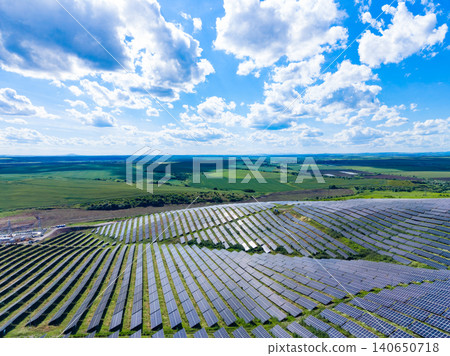 Solar panels cover a large area in a green landscape under a bright sky with clouds during daytime Solar panels cover a large area in a green landscape under a bright sky with clouds during daytime 140650718