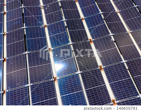 Views of solar panels installed on a rooftop in a sunny location during the daytime showing multiple rows in a grid pattern 140650781