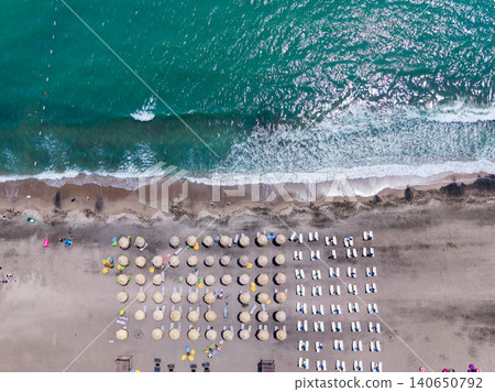 People enjoy a sunny day at the beach with umbrellas, sun loungers, and waves crashing on the shore during midday People enjoy a sunny day at the beach with umbrellas, sun loungers, and waves crashing on the shore during midday 140650792