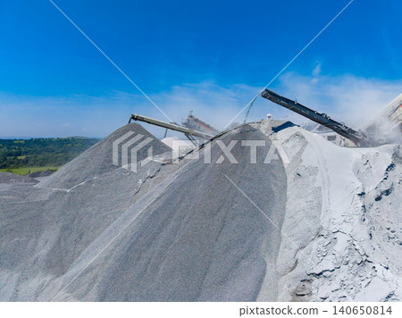 Granite quarry with large piles of stone being processed under a clear blue sky in a rural location during daytime hours Granite quarry with large piles of stone being processed under a clear blue sky in a rural location during daytime hours 140650814