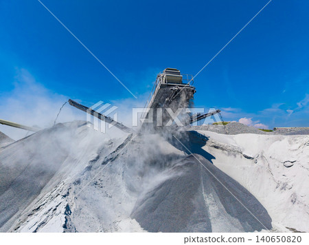 Heavy machinery works in a granite quarry with dust and stone piles under a bright blue sky Heavy machinery works in a granite quarry with dust and stone piles under a bright blue sky 140650820