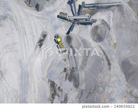 Granite quarry activity with machinery and equipment moving stone materials in a large open pit during daylight hours Granite quarry activity with machinery and equipment moving stone materials in a large open pit during daylight hours 140650822