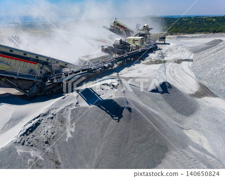 Granite quarry processing equipment at work in a large site producing stone material in an open area during daytime Granite quarry processing equipment at work in a large site producing stone material in an open area during daytime 140650824