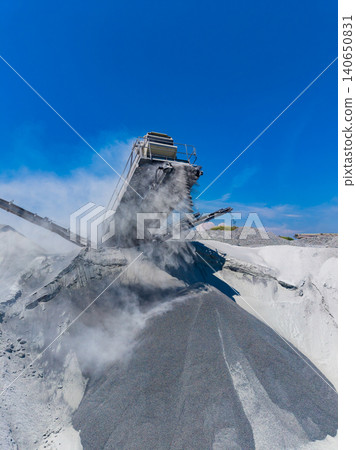 Granite quarry operation takes place under a clear blue sky with equipment processing rocks and producing granite dust Granite quarry operation takes place under a clear blue sky with equipment processing rocks and producing granite dust 140650831