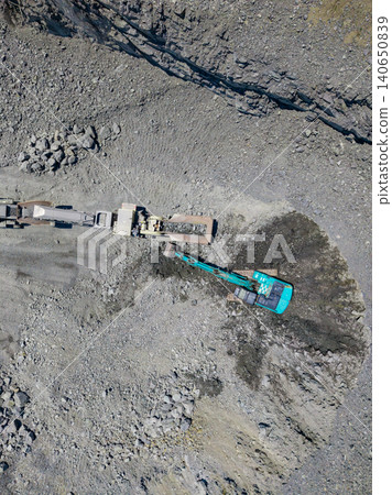 Workers in a granite quarry use heavy machinery to extract rocks and stones from the earth for construction and landscaping purposes during the day Workers in a granite quarry use heavy machinery to extract rocks and stones from the earth for construction and landscaping purposes during the day 140650839
