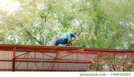 Roofer working in special protective work wear gloves, using air or pneumatic nail gun installing asphalt shingle on top of the new roof, Concept of residential building under construction. Roofer working in special protective work wear gloves, using air or pneumatic nail gun installing asphalt shingle on top of the new roof, Concept of residential building under construction. 140650893