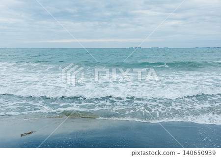 Waves crash on the shore as clouds fill the sky over a quiet beach near the ocean during a calm afternoon Waves crash on the shore as clouds fill the sky over a quiet beach near the ocean during a calm afternoon 140650939
