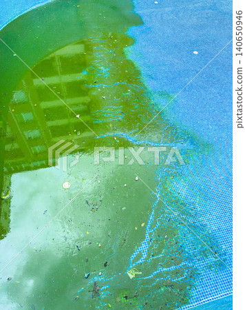Water collects in a pool with green algae and debris near a building on a cloudy day in an urban area Water collects in a pool with green algae and debris near a building on a cloudy day in an urban area 140650946