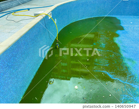 Water in a swimming pool shows green algae growth with a hose for draining located at a property site in mid-afternoon light Water in a swimming pool shows green algae growth with a hose for draining located at a property site in mid-afternoon light 140650947