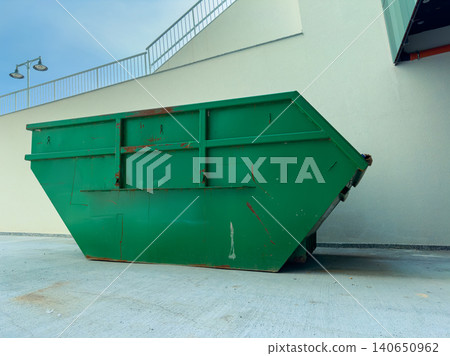 Large green dumpster placed near a building on a concrete surface under a clear sky during the daytime Large green dumpster placed near a building on a concrete surface under a clear sky during the daytime 140650962