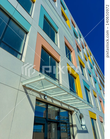 Colorful building with large windows and glass entrance in a city setting during daytime with clear blue sky above 140650972