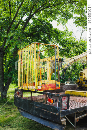 Closeup yellow safety cage on flatbed with hydraulic arm and rusted mesh, textured paint and metal details, shadowed trees framing background, utilitarian aesthetic Closeup yellow safety cage on flatbed with hydraulic arm and rusted mesh, textured paint and metal details, shadowed trees framing background, utilitarian aesthetic 140651014