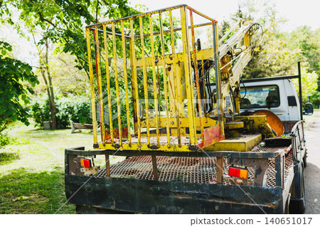 Sunlit utility truck with safety cage, yellow metal cage mounted on bed, boom lowered, grassy avenue, quiet midday atmosphere, inspectionready equipment with subtle wear Sunlit utility truck with safety cage, yellow metal cage mounted on bed, boom lowered, grassy avenue, quiet midday atmosphere, inspectionready equipment with subtle wear 140651017